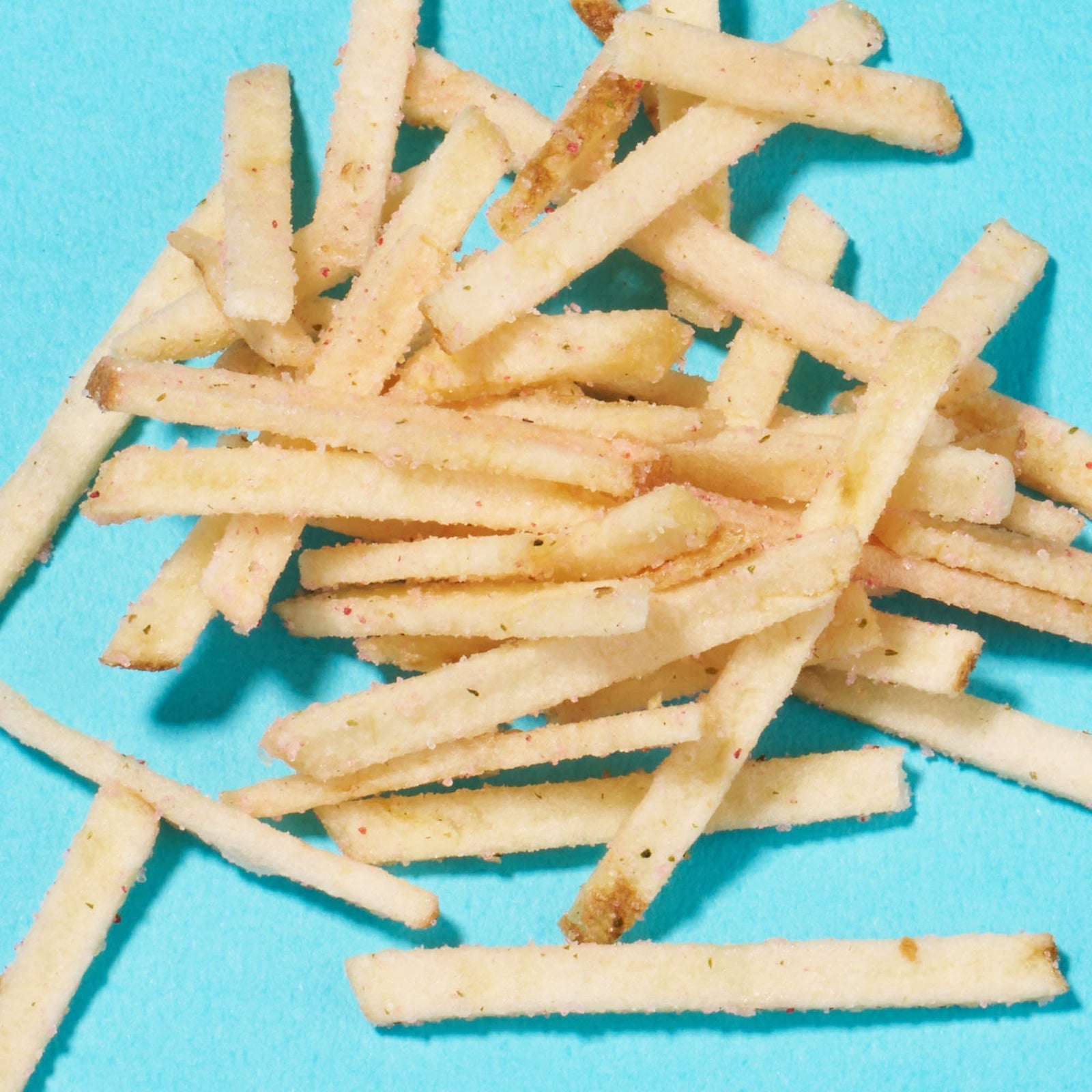 A pile of thin, crispy French fries on a bright blue background, evoking the unique treats from the Bokksu Snack Box: Seasons of Japan.